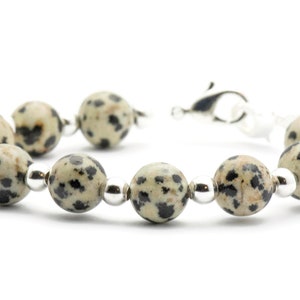 May include: A bracelet made with black and white dalmatian jasper beads and silver spacer beads. The bracelet has a silver clasp.