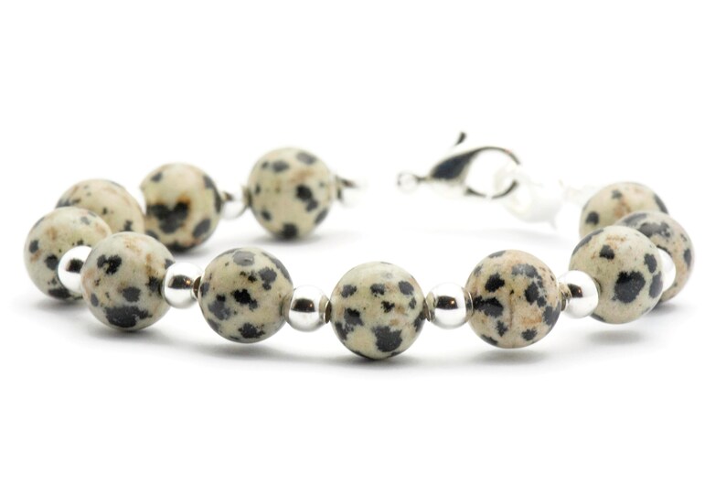 May include: A bracelet made with black and white dalmatian jasper beads and silver spacer beads. The bracelet has a silver clasp.