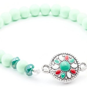 May include: A light green beaded bracelet with a silver charm featuring a green, red and white flower design.