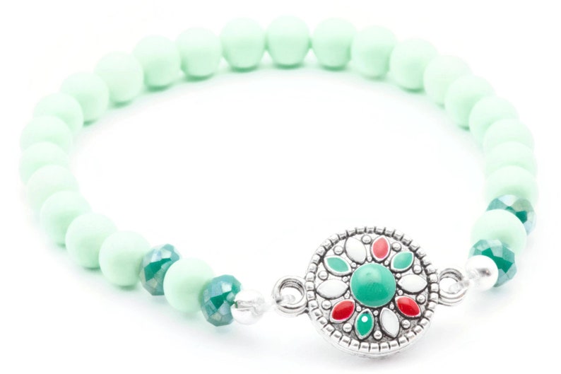 May include: A light green beaded bracelet with a silver charm featuring a green, red and white flower design.
