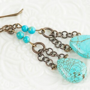 May include: Turquoise dangle earrings with a chain and turquoise beads. The earrings are made of metal and have a teardrop shape.