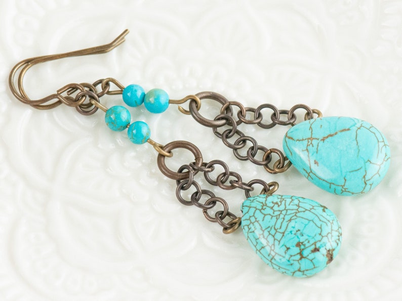 May include: Turquoise dangle earrings with a chain and turquoise beads. The earrings are made of metal and have a teardrop shape.