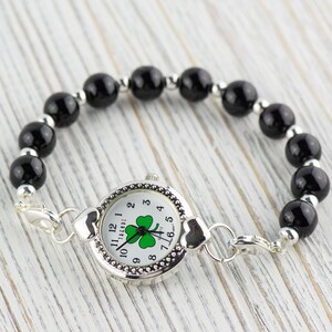 Peut inclure: Un bracelet en perles noires avec un cadran de montre argent&eacute; orn&eacute; d'un tr&egrave;fle &agrave; quatre feuilles. Le cadran de la montre comporte des chiffres romains blancs et un tr&egrave;fle vert au centre.