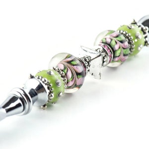 Peut inclure: Un ouvre-lettre en argent avec un manche d&eacute;coratif en perles de verre vertes et roses. Le manche est &eacute;galement orn&eacute; d'un charme en argent.