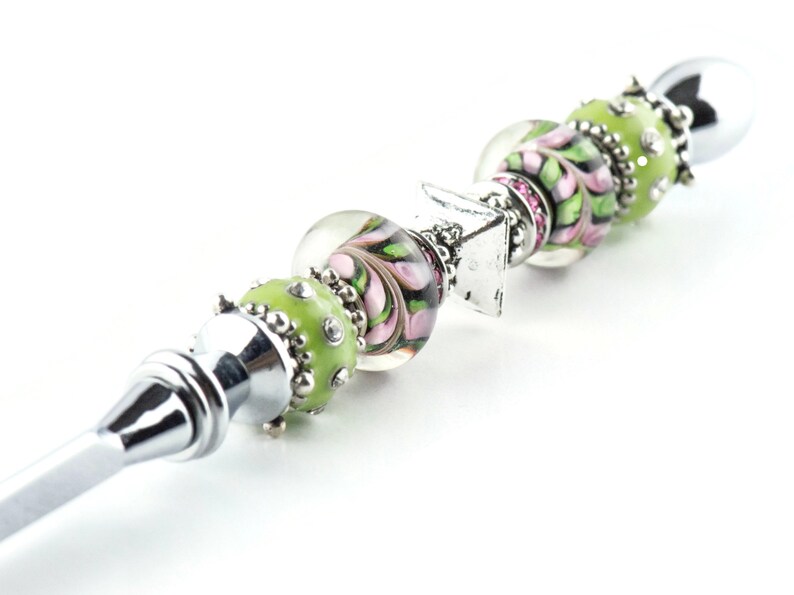 Peut inclure: Un ouvre-lettre en argent avec un manche d&eacute;coratif en perles de verre vertes et roses. Le manche est &eacute;galement orn&eacute; d'un charme en argent.