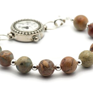 May include: A silver watch with a white face and black hands is attached to a bracelet made of brown, green, and red patterned beads.