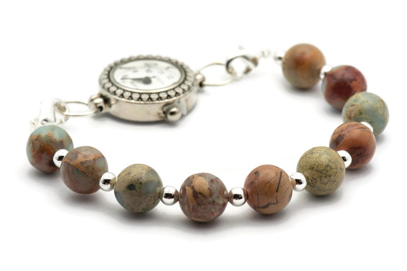 May include: A silver watch with a white face and black hands is attached to a bracelet made of brown, green, and red patterned beads.