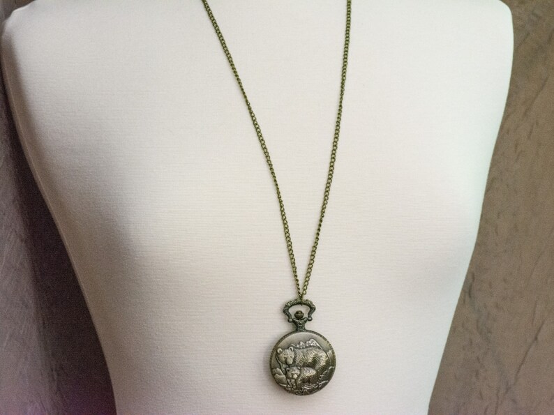 May include: A bronze chain necklace with a round pendant featuring an engraved image of two bears. The pendant is attached to the chain with a small loop.