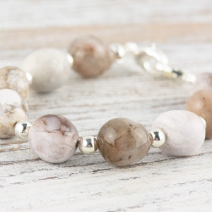 May include: A bracelet made with light brown and white agate beads and silver spacers. The bracelet has a silver clasp.
