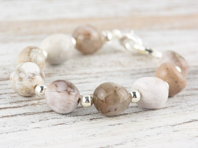 May include: A bracelet made with light brown and white agate beads and silver spacers. The bracelet has a silver clasp.