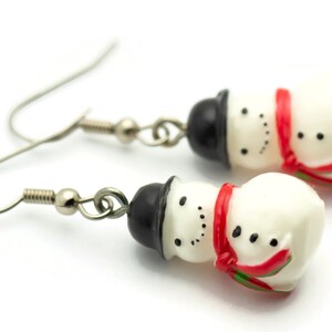 May include: A pair of silver snowman earrings with black hats and red scarves. The snowmen are white with black eyes and buttons.