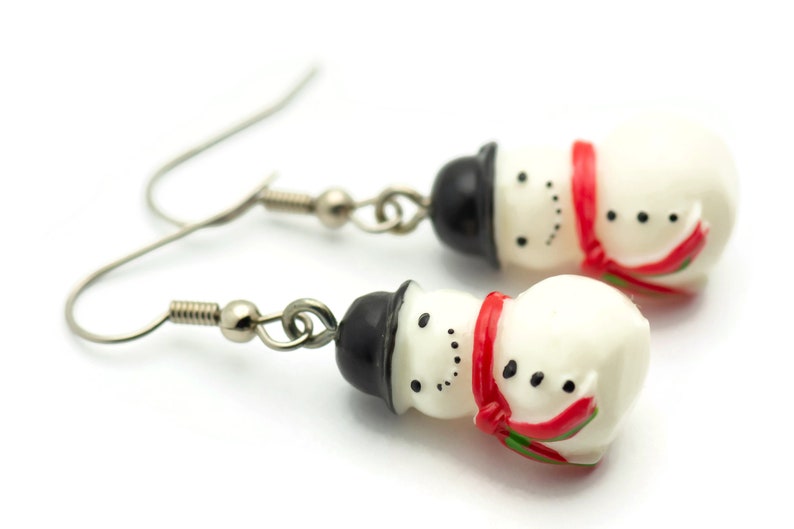 May include: A pair of silver snowman earrings with black hats and red scarves. The snowmen are white with black eyes and buttons.