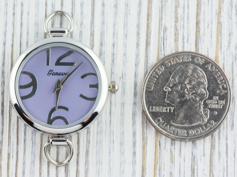 May include: A silver pocket watch with a purple face and black Roman numeral hour markers. The watch has a silver loop on the top and a silver clasp on the bottom.