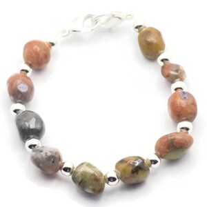 May include: A bracelet made with brown, gray, and orange stones with silver beads and a silver clasp.
