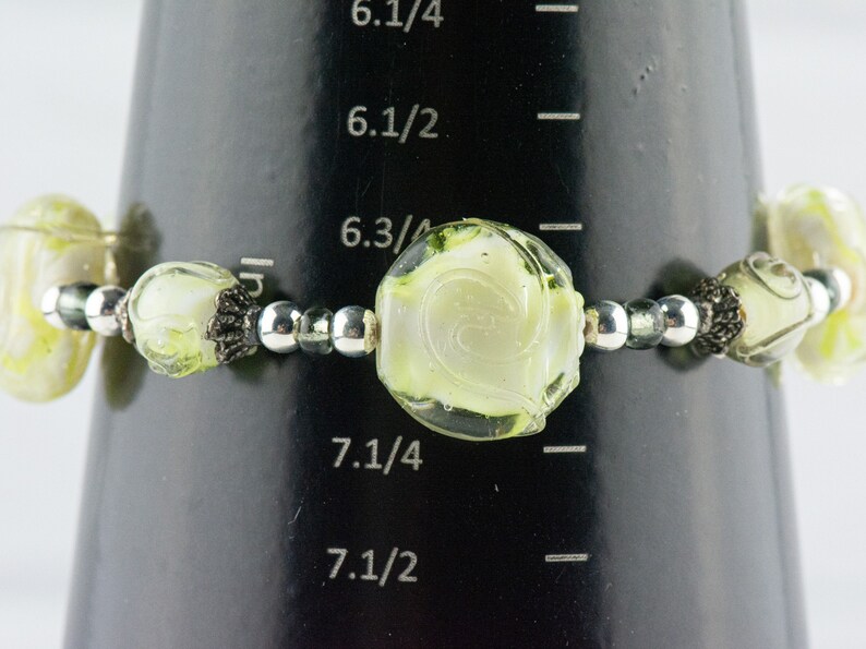 Peut inclure: Un bracelet en verre vert et blanc avec des perles argent&eacute;es. Le bracelet a une circonf&eacute;rence de 7 1/4 pouces.