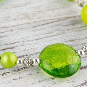 Puede incluir: Un brazalete de cuentas de vidrio verde con cuentas espaciadoras plateadas. El brazalete presenta una cuenta de vidrio verde grande, redonda y con una superficie texturizada.