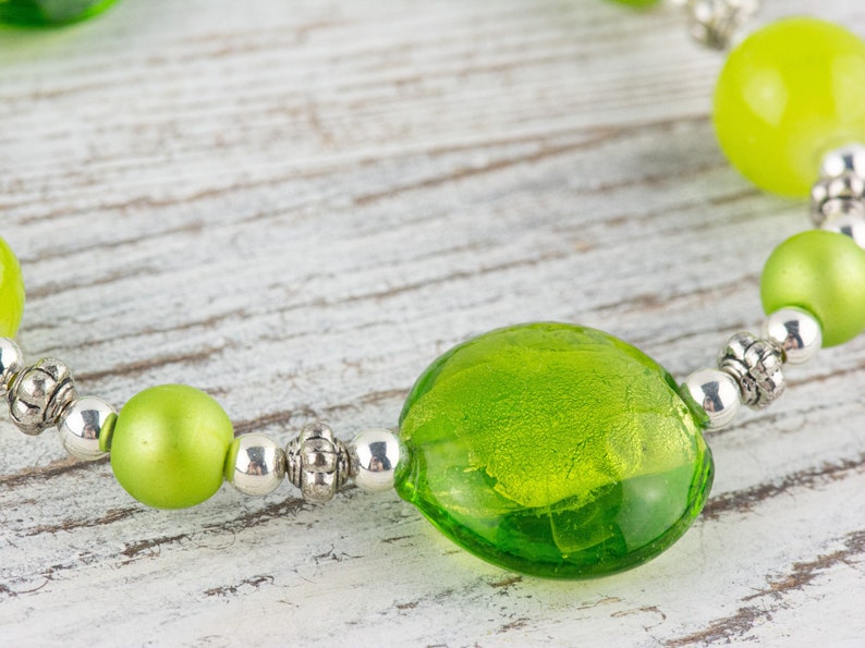 Puede incluir: Un brazalete de cuentas de vidrio verde con cuentas espaciadoras plateadas. El brazalete presenta una cuenta de vidrio verde grande, redonda y con una superficie texturizada.