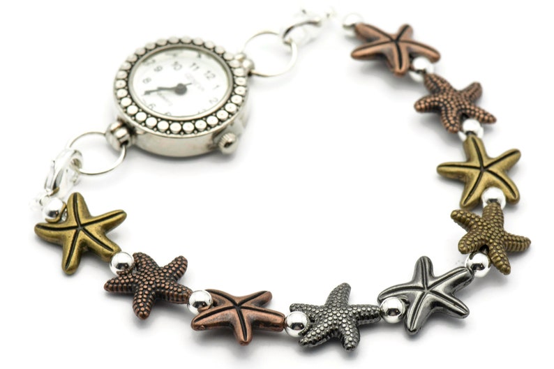 May include: A silver watch with a white face and black hands is attached to a bracelet with silver and bronze starfish charms.