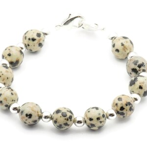 May include: A bracelet made with dalmatian jasper beads and silver spacers. The bracelet has a silver clasp.