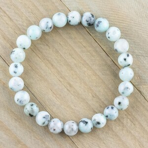 Puede incluir: Un brazalete de cuentas de piedra con manchas blancas y negras. El brazalete est&aacute; hecho de cuentas redondas y est&aacute; enhebrado en un cord&oacute;n el&aacute;stico transparente.