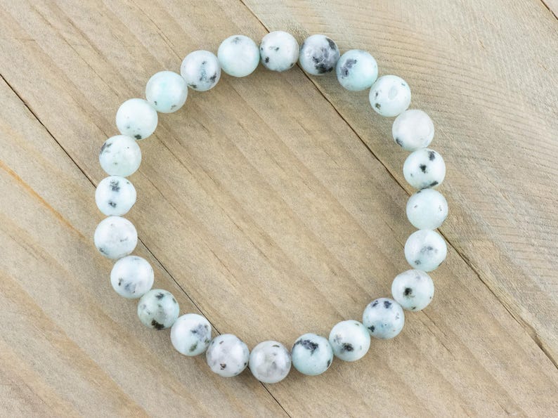 Puede incluir: Un brazalete de cuentas de piedra con manchas blancas y negras. El brazalete est&aacute; hecho de cuentas redondas y est&aacute; enhebrado en un cord&oacute;n el&aacute;stico transparente.