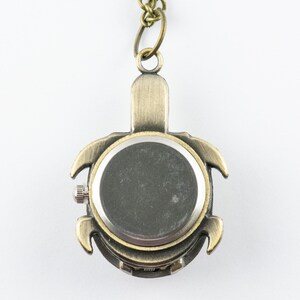 May include: A bronze turtle-shaped pocket watch with a silver back. The watch is on a chain.