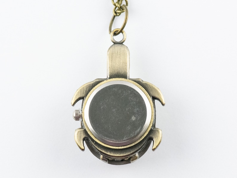 May include: A bronze turtle-shaped pocket watch with a silver back. The watch is on a chain.