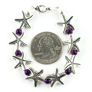 May include: A silver bracelet with a series of starfish charms and purple beads. The bracelet is about the size of a US quarter.