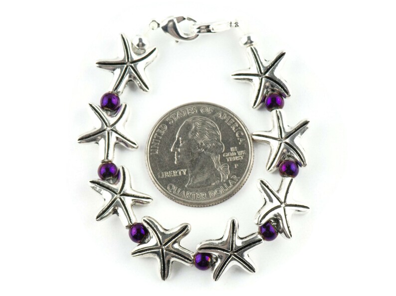 May include: A silver bracelet with a series of starfish charms and purple beads. The bracelet is about the size of a US quarter.