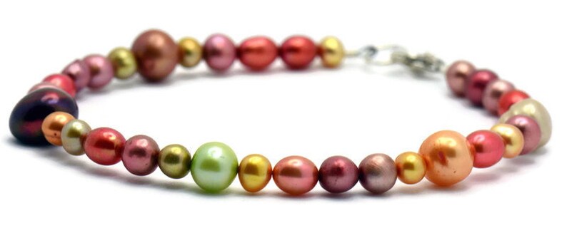 Pu&ograve; includere: Un braccialetto di perle multicolori con una chiusura argentata. Le perle sono in tonalit&agrave; di rosa, verde e marrone.