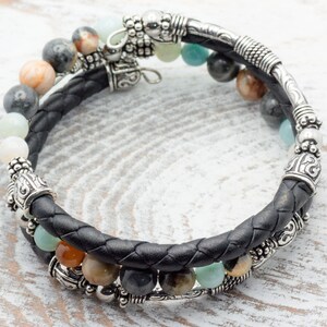 May include: A black leather bracelet with silver beads and charms. The bracelet features a variety of stones, including green, brown, and white.