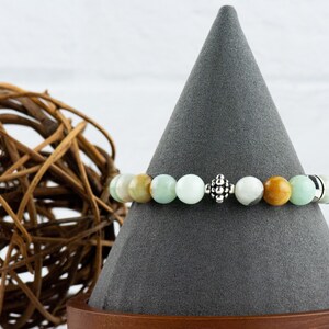 Black Gold Amazonite Genuine Gemstone Stretch Bracelet displayed on a decorative black bracelet stand. Amazonite beads are multicolor earth-tones. Center bead is a silver Bali style bead.