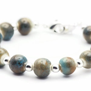 Pode incluir: Um bracelete feito de contas de cer&acirc;mica azul e marrom com espa&ccedil;adores prateados.