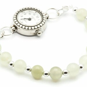 May include: A silver watch with a white face and black hands attached to a bracelet of white beads and silver spacers.
