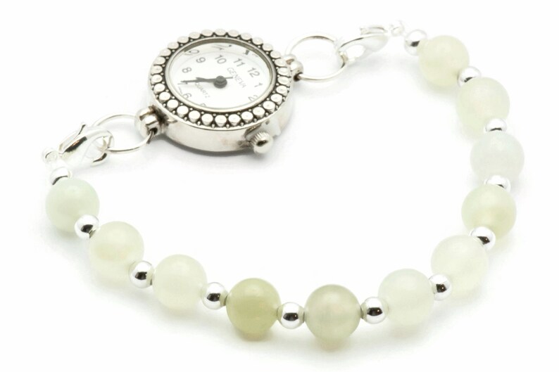 May include: A silver watch with a white face and black hands attached to a bracelet of white beads and silver spacers.