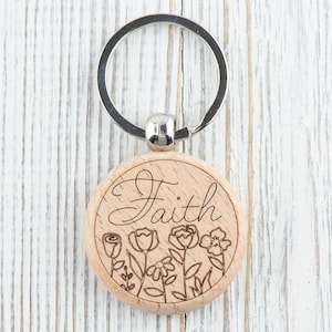 May include: Wooden keyring with a silver ring and a round wooden charm. The charm has the word "Faith" engraved on it, along with a floral design.