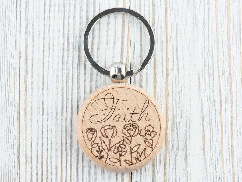 May include: Wooden keyring with a silver ring and a round wooden charm. The charm has the word "Faith" engraved on it, along with a floral design.