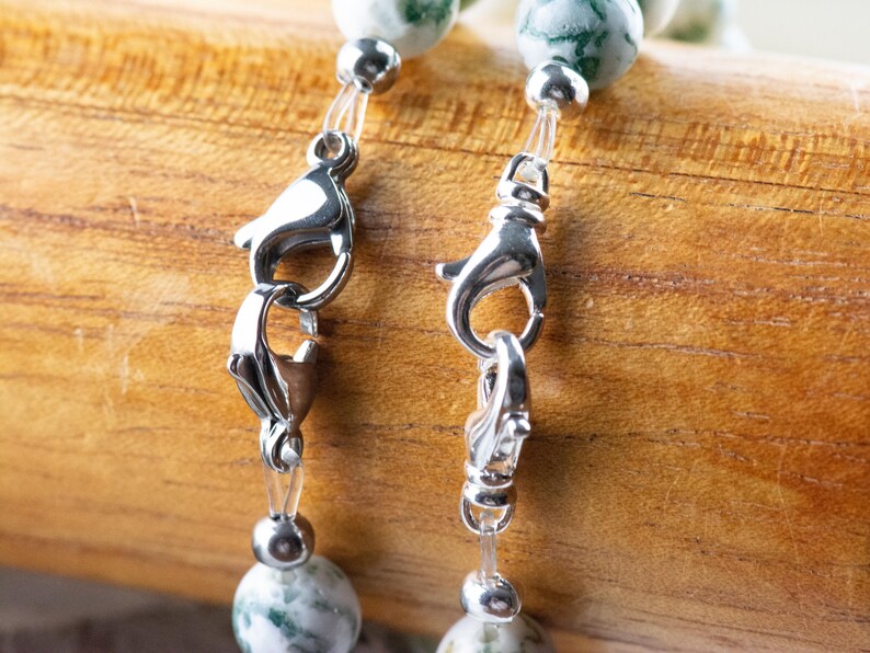 May include: Close-up of a silver clasp on a green and white agate beaded necklace. The clasp is made of metal and has a spring-loaded mechanism.