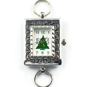 Op de afbeelding: Zilveren zakhorloge met een kerstboomontwerp op de wijzerplaat. Het horloge heeft een zilveren ketting en een decoratieve rand.