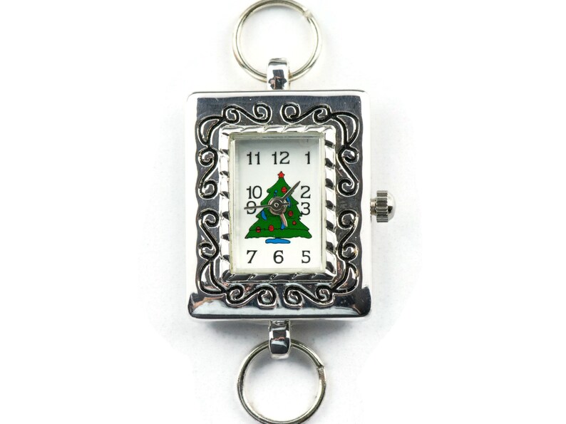 Op de afbeelding: Zilveren zakhorloge met een kerstboomontwerp op de wijzerplaat. Het horloge heeft een zilveren ketting en een decoratieve rand.