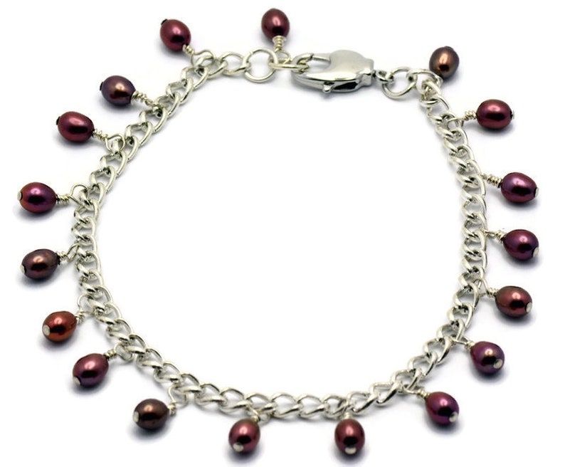 May include: A silver chain bracelet with a lobster clasp and multiple dangling maroon pearls.