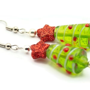 Op de afbeelding: Een paar groene glazen kerstboom oorbellen met rode glittersterren. De oorbellen zijn zilver en hebben een haak sluiting.