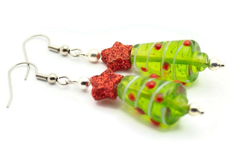 Op de afbeelding: Een paar groene glazen kerstboom oorbellen met rode glittersterren. De oorbellen zijn zilver en hebben een haak sluiting.