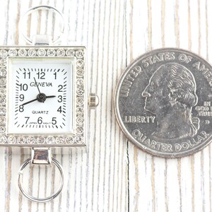 May include: A silver-toned quartz watch with a rectangular face, surrounded by rhinestones. The watch face is white with black numerals and hands. The word "GENEVA" is printed on the watch face. A U.S. quarter is next to the watch.