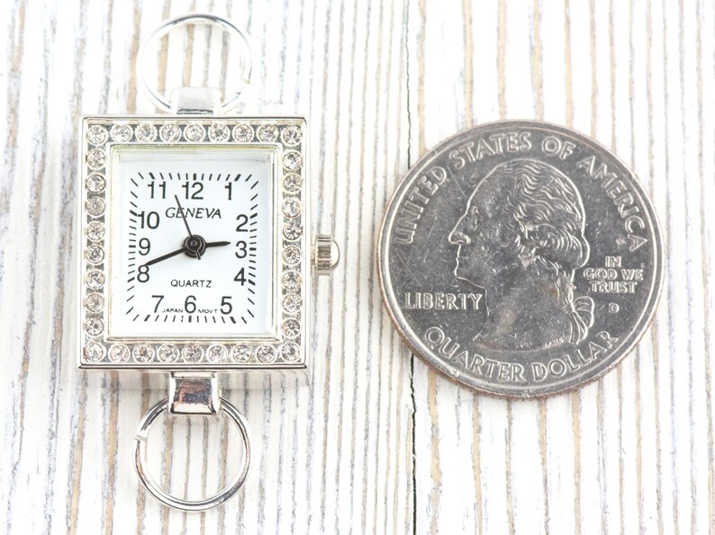 May include: A silver-toned quartz watch with a rectangular face, surrounded by rhinestones. The watch face is white with black numerals and hands. The word "GENEVA" is printed on the watch face. A U.S. quarter is next to the watch.