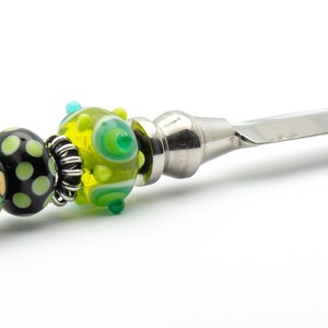 May include: A silver letter opener with a handle decorated with green, black, and gold glass beads.