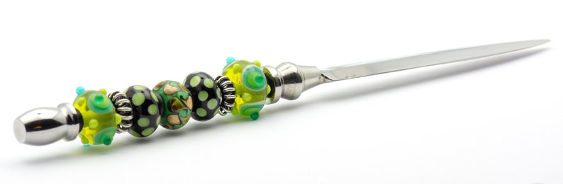 May include: A silver letter opener with a handle decorated with green, black, and gold glass beads.