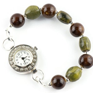 May include: A silver wristwatch with a white face and black hands. The watch is attached to a bracelet made of brown and green ceramic beads.