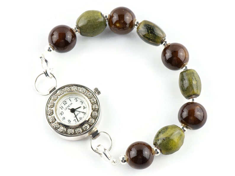 May include: A silver wristwatch with a white face and black hands. The watch is attached to a bracelet made of brown and green ceramic beads.