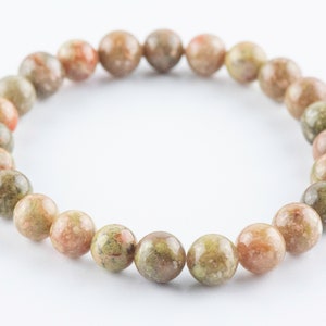 May include: A bracelet made of round, green, brown, and pink speckled beads.